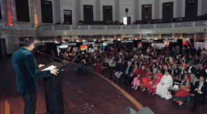 Speaker addressing a large audience during a multicultural community event in an auditorium setting