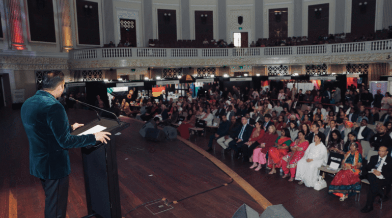Speaker addressing a large audience during a multicultural community event in an auditorium setting